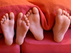 zwei Paar Füße unter einer roten Bettdecke